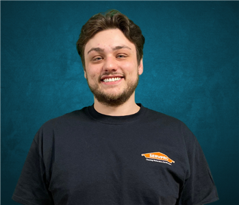 Male employee with brown hair smiling in front of a blue background. 