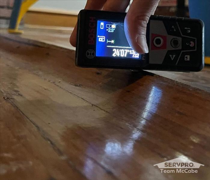 a hand holding a device with a moisture reading, over top of a hardwood floor rising up 